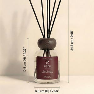 Peut inclure: Diffuseur de parfum en verre avec un dessus en bois fonc&eacute; et des b&acirc;tonnets noirs. L'&eacute;tiquette indique "Ruby Cherry" avec des notes de cerise, de prune et de vanille. Hauteur 10,8 cm, diam&egrave;tre 6,5 cm, hauteur totale 24,5 cm.