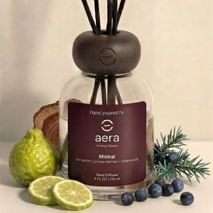 May include: A clear glass reed diffuser with a dark brown cap and black reeds. The label reads "Mistral" and lists bergamot, juniper berries, and cedarwood. The diffuser is 4 fl oz / 120 ml. The image includes a green citrus fruit and juniper berries.
