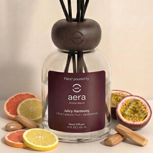 Pode incluir: Um difusor de cana de vidro transparente com uma tampa e varetas de madeira castanha escura. O rótulo diz "Juicy Harmony" com aromas de citrinos, maracujá e sândalo. Fatias de toranja, limão e maracujá são dispostas ao redor do difusor. Contém 120 ml.