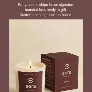 May include: A white frosted glass candle with a lit wick and a dark brown label reading Aera Aroma Atelier, 7 oz (198 g). Beside it sits a dark brown box with the Aera logo and a matching dark brown lid. Text above reads: The gift that arrives already beautiful. No wrapping needed. Every candle ships in our signature branded box, ready to gift. Custom message card included.