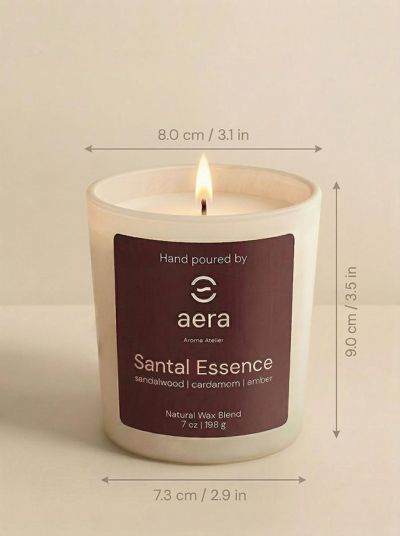 May include: A lit candle in a frosted glass jar with a dark label reading Hand poured by aera Aroma Atelier Santal Essence sandalwood | cardamom | amber Natural Wax Blend 7 oz. The jar measures 3.1 inches wide at the top, 2.9 inches at the base, and 3.5 inches tall.