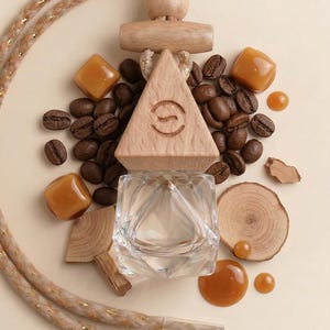 May include: A clear glass car air freshener with a wooden triangle top and a decorative rope. The image includes coffee beans, caramel candies, and wood slices, creating a warm, inviting aesthetic. The air freshener has a geometric design.