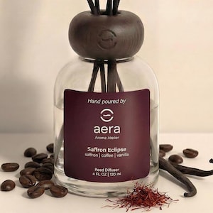 May include: A clear glass reed diffuser with a dark brown wooden top and reeds. The label reads "Saffron Eclipse" and "4 FL OZ | 120 ml". Coffee beans, saffron threads, and vanilla beans are scattered around the base.