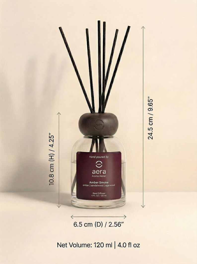 K&ouml;nnte beinhalten: Ein klarer Glas-Reed-Diffusor mit einem dunkelbraunen Holzaufsatz und Schilf. Auf dem Etikett steht "aera Aroma Atelier Amber Smoke". Der Diffusor ist 10,8 cm hoch und 6,5 cm im Durchmesser, mit einem Nettoinhalt von 120 ml.