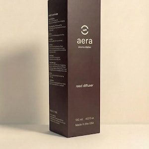 K&ouml;nnte beinhalten: Dunkelbraune rechteckige Schachtel f&uuml;r einen Reed-Diffusor. Der Markenname "aera" und "Aroma Atelier" sind in Wei&szlig; geschrieben. Auf der Schachtel steht "Reed Diffusor" und das Volumen betr&auml;gt 120 ml. Hergestellt in den USA.