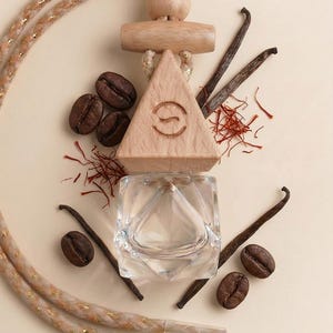 May include: A wooden car air freshener with a triangular design and a clear glass container. The image includes coffee beans, vanilla pods, and saffron threads, suggesting a fragrance theme. The air freshener hangs from a rope.