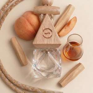 May include: An arrangement of natural elements including a peach, wooden triangle with a symbol, wooden sticks, a small glass container, and a clear glass perfume bottle with a brown liquid. A rope with gold accents is also present.