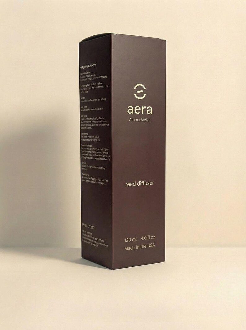 May include: A dark brown rectangular box for a reed diffuser, branded with "aera" and "Aroma Atelier" in white. The box states a volume of 120 ml (4.0 fl oz) and "Made in the USA". Safety warnings are printed on the side of the box.