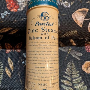 Può includere: Latta di polvere Puretest Zinc Stearate vintage con Balsamo del Perù. Il contenitore cilindrico ha un coperchio blu e un corpo beige con testo e grafica stampati. Il prodotto è una polvere lenitiva per la pelle irritata.