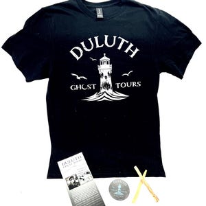 May include: Black t-shirt with a white graphic of a lighthouse and the words "Duluth Ghost Tours". Includes a brochure, sticker, and two sticks. The shirt is made of a soft material.