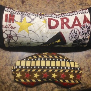 May include: A black and cream-colored pillow with the words "IN DRAMA theatre Romance" and film reel graphics. Below is a matching eye mask with a film strip and star pattern.