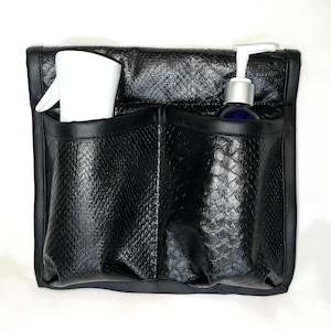 May include: A black faux leather utility pouch with a textured snakeskin pattern, featuring two large front pockets. One pocket contains a white spray bottle, and the other contains a dark blue bottle with a white pump dispenser top.