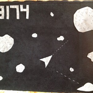 Puede incluir: Funda negra para portátil con diseño espacial. Presenta parches blancos irregulares que simulan asteroides, una flecha blanca y el texto "3174 LIE" en letras blancas. Una línea de puntos sugiere una trayectoria.