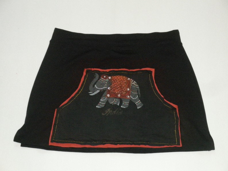 以下が含まれることがあります： 象の刺繍が施された黒いスカート。象はグレーで、赤とオレンジのアクセントがあり、下に「India」の文字が書かれています。デザインは赤い縁取りで囲まれています。