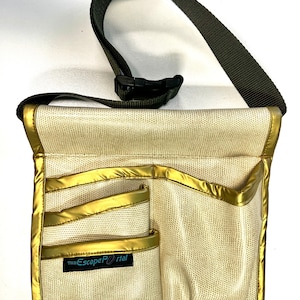 May include: A beige fanny pack with gold trim and multiple pockets. The bag has a textured pattern and a black adjustable strap. The text "The Escape Portal" is on a small black tag on the front of the bag.