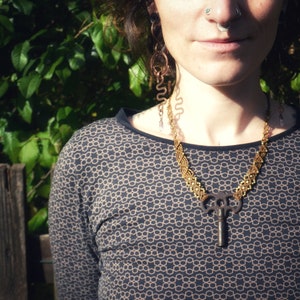 Könnte beinhalten: Eine Person trägt ein schwarzes Shirt mit einer braunen und goldenen Schlüsselkette. Die Kette ist aus geflochtener Schnur und hat einen kleinen Schlüsselanhänger unten.