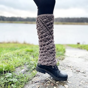 May include: Brown crocheted leg warmers with a textured pattern. The leg warmers are worn over black leggings and reach to the knee.