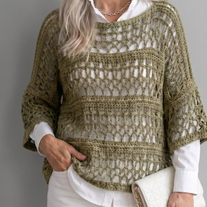 May include: Olive green crochet top with a loose, open weave design. The top has a round neckline and three-quarter length sleeves. The crochet pattern creates a textured, airy look. The top is worn over a white collared shirt.