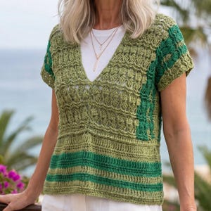 May include: A green crochet top with a V-neck design. The top features varying shades of green, with a striped pattern at the bottom and a textured pattern on the upper portion. The short-sleeved top is handmade.