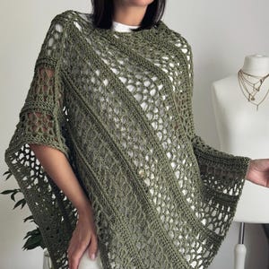 Può includere: Un poncho all'uncinetto color verde oliva caratterizzato da un motivo a rete traforato intervallato da fasce diagonali piene. Il capo presenta una silhouette ampia e drappeggiata con ampie aperture per le braccia e una trama in filato.