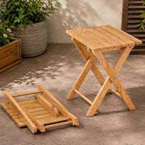May include: Two light brown wooden stools with a slatted top design. One stool is fully assembled in an upright position with crossed legs, while the other stool is folded flat, showing the hinges and the underside of the slatted seat surface.