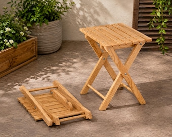 May include: Two light brown wooden stools with a slatted top design. One stool is fully assembled in an upright position with crossed legs, while the other stool is folded flat, showing the hinges and the underside of the slatted seat surface.