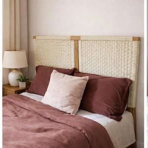 May include: A bedroom scene featuring a bed with a woven headboard and bedding in shades of mauve and cream. The bed is made with a mauve duvet cover, matching pillowcases, and a light pink accent pillow. A cream-colored sheet is visible.