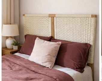 May include: A bedroom scene featuring a bed with a woven headboard and bedding in shades of mauve and cream. The bed is made with a mauve duvet cover, matching pillowcases, and a light pink accent pillow. A cream-colored sheet is visible.