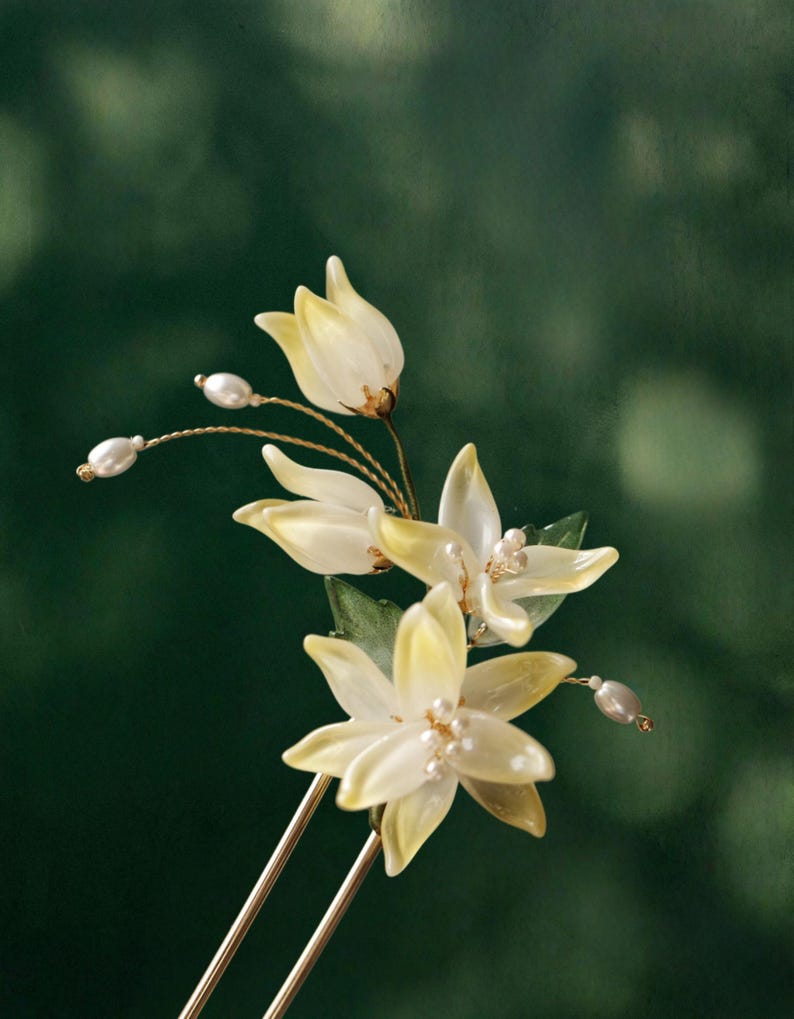 May include: A floral hair accessory featuring delicate, pale yellow flower petals with pearl accents. The flowers are attached to a gold-toned metal hair pin, creating an elegant and natural look.