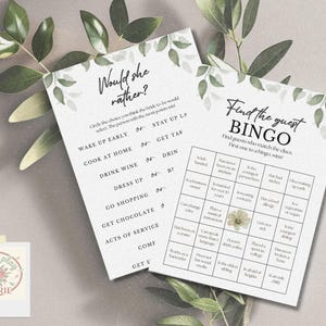 May include: Two white paper game cards with green leaf accents. One card reads "Would she rather?" with choices. The other card is a bingo game. The cards are for a bridal shower.