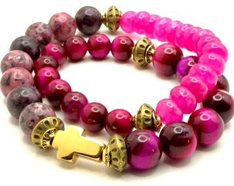 Könnte beinhalten: Drei Armbänder mit Perlen in Rosa-, Lila- und Goldtönen. Die Armbänder haben runde Perlen in verschiedenen Größen und Farben, darunter ein leuchtendes Pink, ein tiefes Lila und goldene Akzente. Ein Armband hat ein goldenes Kreuz.