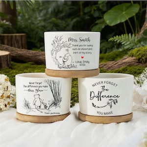 Peut inclure: Trois pots de fleurs en céramique blanche avec des soucoupes en bois. Chaque pot présente un graphisme et un texte noirs différents. L'un dit "Mrs. Smith" avec une illustration de Winnie l'ourson. Un autre dit "N'oubliez jamais la différence que vous faites Mme Gloria". Le troisième dit "N'oubliez jamais la différence que vous faites".