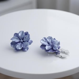 Peut inclure: Une paire de boucles d'oreilles bleues en forme de fleur. Chaque boucle d'oreille présente un motif floral détaillé avec de multiples pétales. Les boucles d'oreilles sont posées sur une surface blanche, mettant en valeur leur savoir-faire et leur couleur.