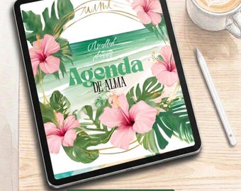 May include: A digital tablet displaying a planner cover with the text Agenda De Alma, decorated with pink hibiscus flowers and green tropical leaves. The screen features a gold circular frame over a green and white background with a stylus nearby.