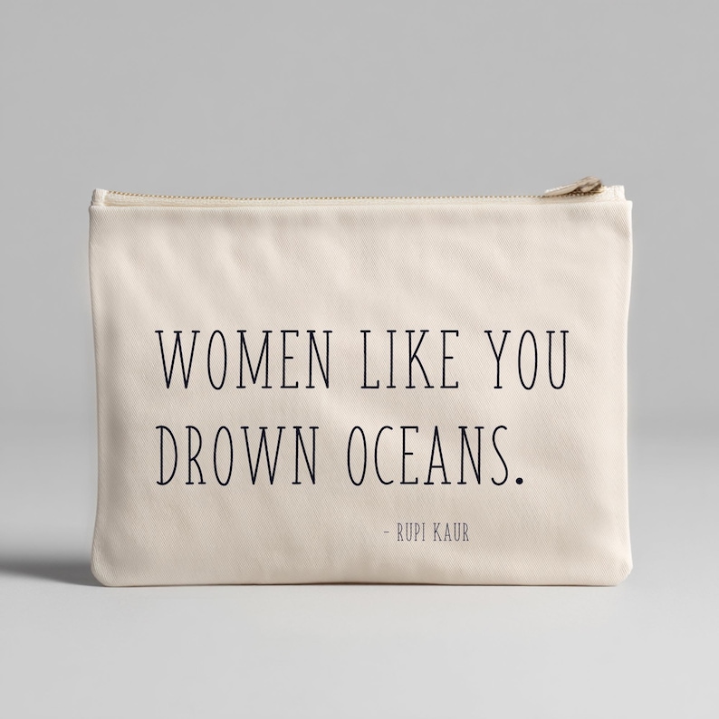 K&ouml;nnte beinhalten: Eine cremefarbene Rei&szlig;verschlusstasche mit dem Text "WOMEN LIKE YOU DROWN OCEANS." und dem Namen des Autors, Rupi Kaur, in Schwarz gedruckt. Die Tasche hat ein schlichtes, minimalistisches Design.