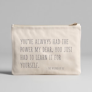 Puede incluir: Bolsa con cremallera de color crema con la cita "YOU'VE ALWAYS HAD THE POWER MY DEAR, YOU JUST HAD TO LEARN IT FOR YOURSELF." de El Mago de Oz. El texto es de color azul marino oscuro.