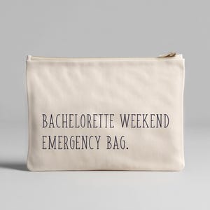 Może przedstawiać: Kremowa, prostokątna kosmetyczka z zamkiem błyskawicznym z czarnym napisem "BACHELORETTE WEEKEND EMERGENCY BAG". Torba wykonana jest z miękkiego, teksturowanego materiału i ma złoty zamek błyskawiczny.
