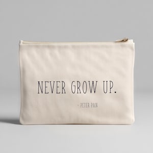 May include: A cream-coloured zippered pouch with the text "NEVER GROW UP." in black, followed by "- PETER PAN" below. The pouch has a rectangular shape and a gold-coloured zipper.