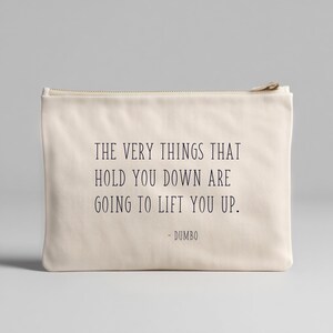 May include: A cream canvas pouch with a zip. The pouch has the quote "THE VERY THINGS THAT HOLD YOU DOWN ARE GOING TO LIFT YOU UP." from Dumbo in dark blue text. A simple and inspirational accessory for everyday use.