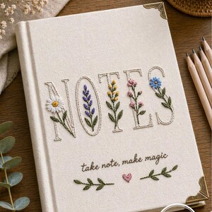 Puede incluir: Cuaderno color crema con detalles florales bordados que deletrean "NOTES". La portada presenta una margarita, lavanda, flores amarillas y azules. El texto "take note, make magic" está bordado debajo. Las esquinas doradas añaden un toque de elegancia.