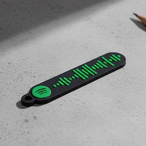 Può includere: Portachiavi nero con codice Spotify e dettagli verdi. Il portachiavi presenta il logo Spotify verde e un motivo a onde sonore verde. Una matita e una graffetta sono anche nell'immagine.