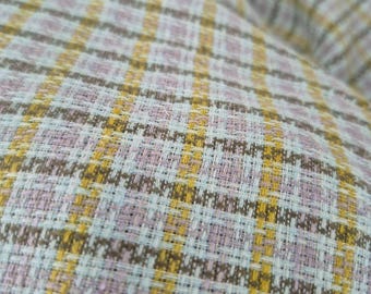 May include: Close-up of a woven fabric with a plaid pattern. The fabric features a combination of colors, including light blue, yellow, brown, and lavender. The plaid design is created by intersecting vertical and horizontal lines.