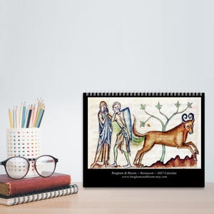 May include: A 2027 calendar featuring a medieval-style illustration of two figures and a horned creature. The text reads Bingham & Bloom ~ Bonnacon ~ 2027 Calendar www.binghamandbloom.etsy.com. The artwork depicts a tan beast with blue horns.
