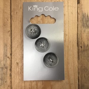 May include: Three grey and white marbled buttons on a silver card with the text "King Cole". The buttons are round with four holes and are displayed on a wooden surface.