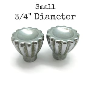 May include: Two small silver-toned metal knobs with a fluted, scalloped edge design and a concave center. The text above the knobs reads Small 3/4" Diameter, indicating the size of these hardware pieces.