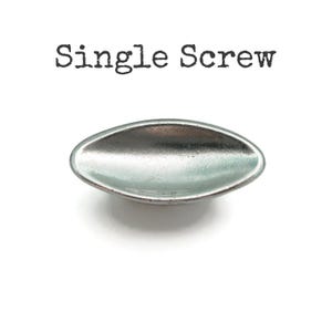 May include: A silver-colored, oval-shaped drawer pull with a slightly concave design. The text "Single Screw" is printed above the pull in a typewriter-style font. The hardware is set against a white background.