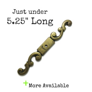 May include: A gold-toned metal decorative piece with a scroll design. It is just under 5.25 inches long.