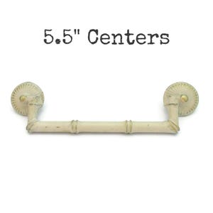 May include: Off-white cabinet pull with a bamboo-style handle and decorative circular end pieces. The text "5.5" Centers" is printed above the pull. The pull is approximately 5.5 inches in length.