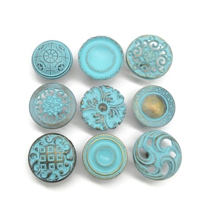 May include: A collection of nine round cabinet knobs in a bright turquoise blue finish with distressed bronze-toned accents. Each knob features a unique circular design, including filigree cutouts, geometric patterns, and embossed floral motifs.