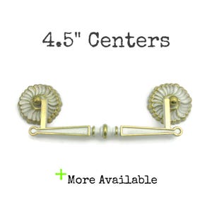 May include: White and gold cabinet hardware with a 4.5" center to center measurement. The hardware has a decorative, scalloped design.